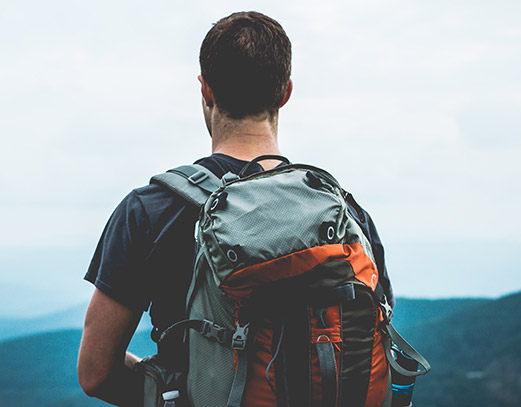 Man outside wearing gray and orange hiker's backpack.