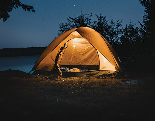 Orange tent illuminated from the inside, under a starry night sky.
